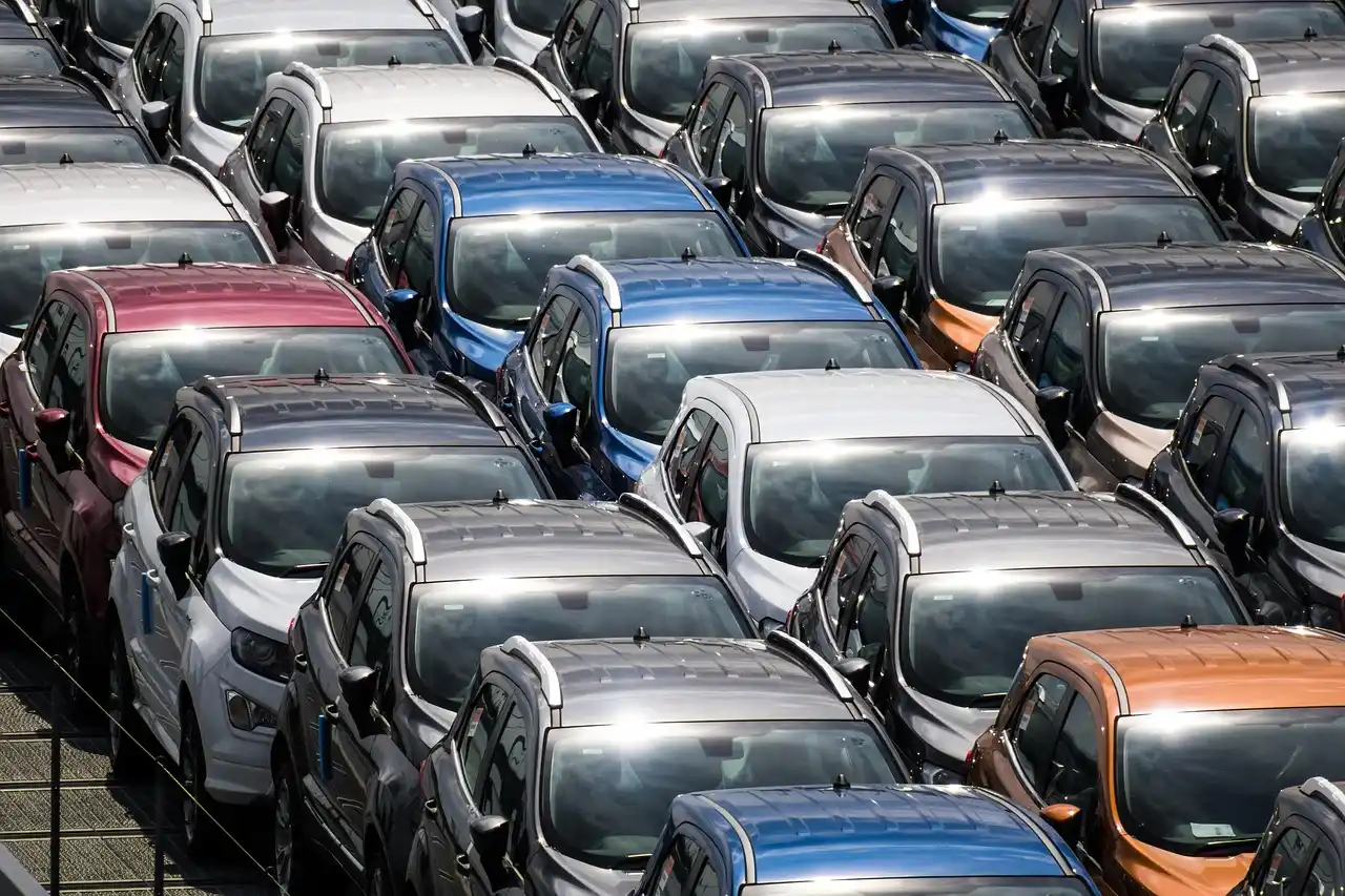 Buyer reviewing a car auction invoice beside a used sedan in an auction lot