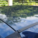 A hail-damaged sedan outside an auto body shop with a mechanic inspecting the roof and hood.