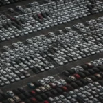 Private seller beside a used sedan outside a car auction yard reviewing paperwork