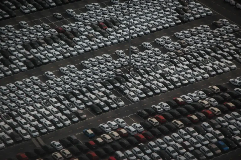 Private seller beside a used sedan outside a car auction yard reviewing paperwork