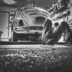 Used car buyer and dealer reviewing paperwork beside a sedan at a dealership lot